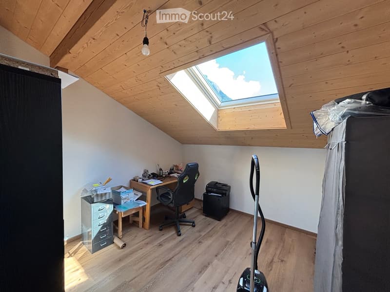 Bright attic room with wooden ceiling and skylight, featuring a desk, chair, printer, and storage cabinet.