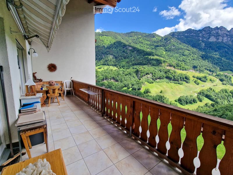 Balcony with wooden railing, tiled floor, and scenic mountain view. Includes a small table, chairs, and a lamp.