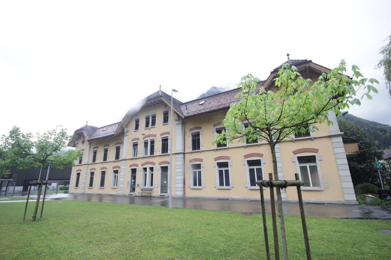 A two-story yellow building with white trim and multiple windows, surrounded by a grassy lawn and trees.