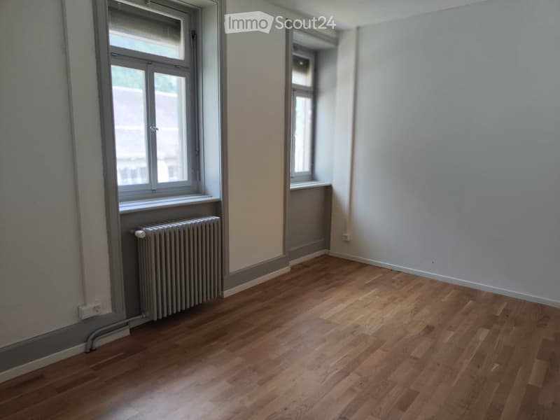 Empty room with wooden flooring, white walls, and two windows with radiators beneath them.