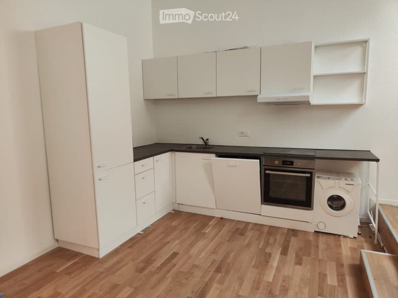 Modern kitchen with white cabinets, black countertops, wooden flooring, and built-in appliances including a sink, oven, dishwasher, and washing machine.