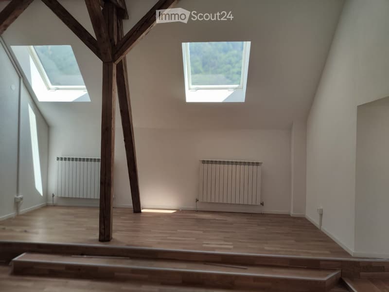 Empty attic room with wooden floors, exposed wooden beams, skylights, and radiators on the walls.