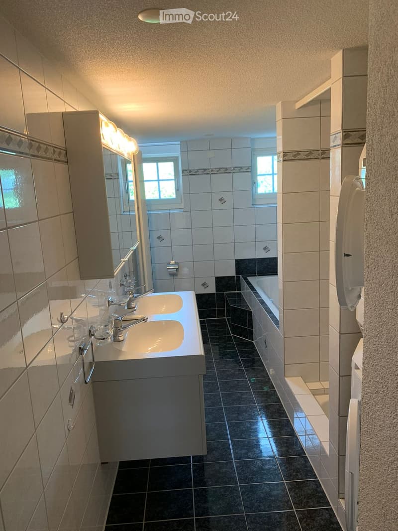 Modern bathroom with double sink, mirror, bathtub, and tiled walls and floor.