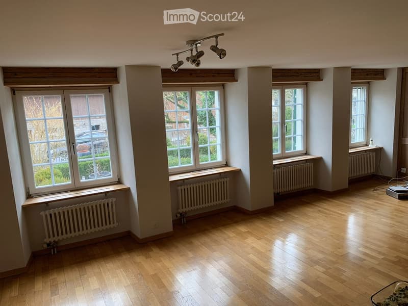 Empty room with wooden flooring, large windows, radiators, and exposed wooden beams on the ceiling.