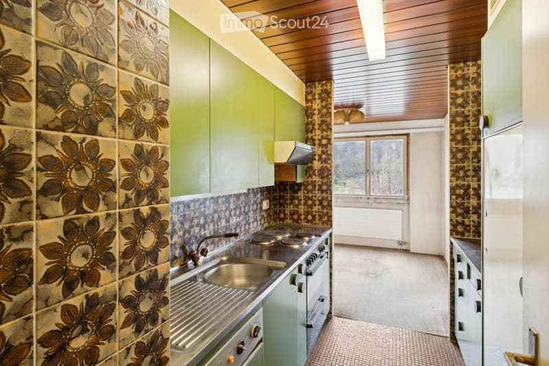 A modern kitchen with green cabinets, tiled walls with flower design, stainless steel sink, oven, and stove, along with a dishwasher