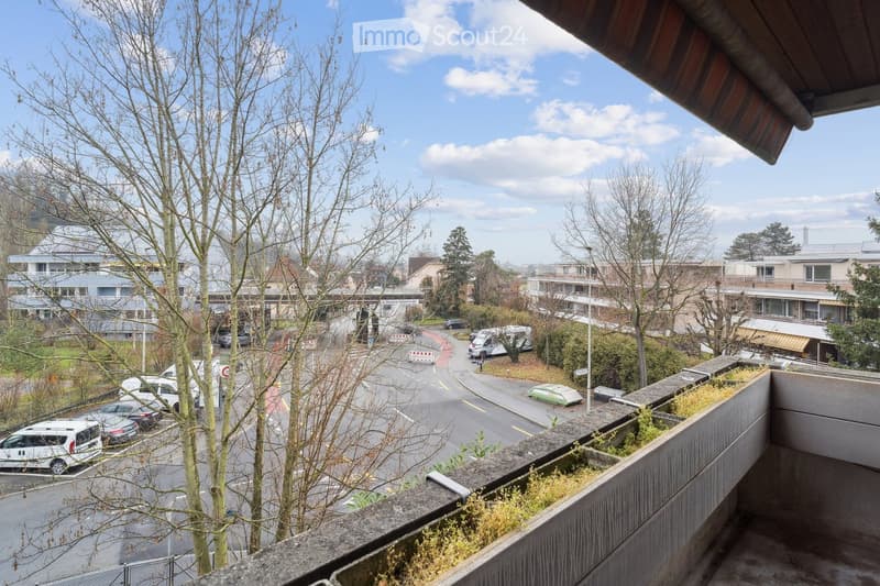 Balcony with view of the parking lot, buildings, and a street with traffic.