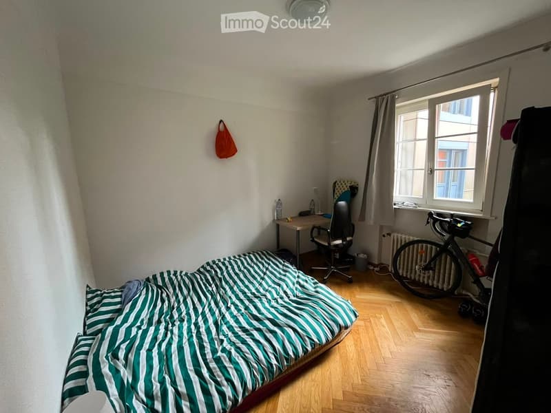 A small bedroom with a bed, a desk, a chair, and a bicycle near the window.