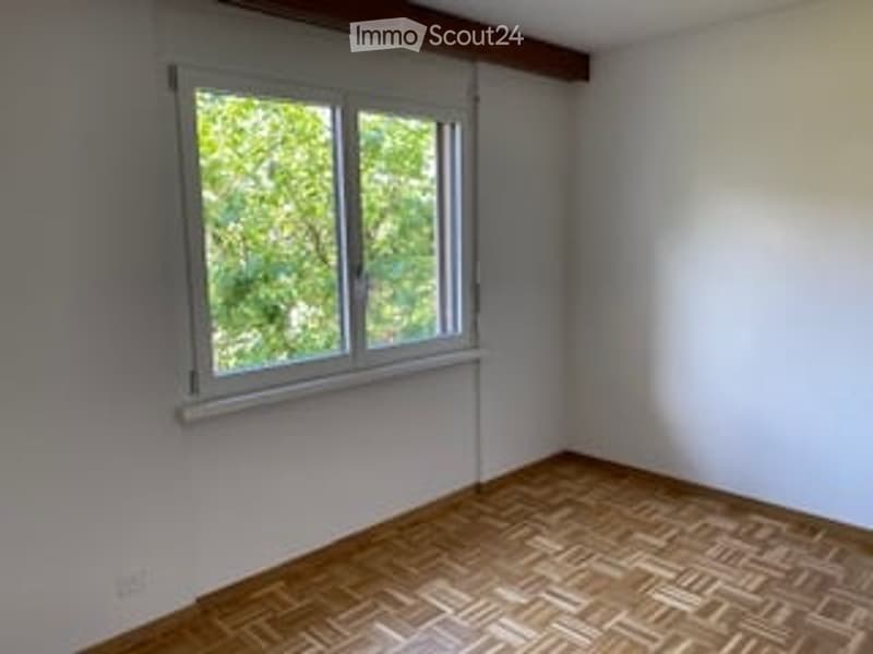 Empty room with wooden parquet flooring, white walls, and a single window with white frame and blinds.