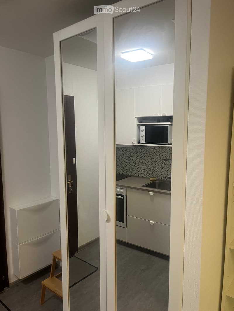 Modern kitchen with white cabinets, microwave, oven, sink, and a small wooden stool near the entrance.