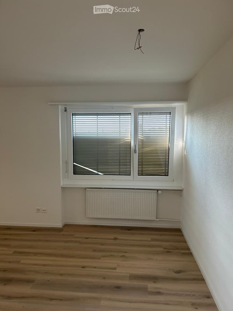Empty room with wooden flooring, white walls, a window with blinds, and a radiator below the window.