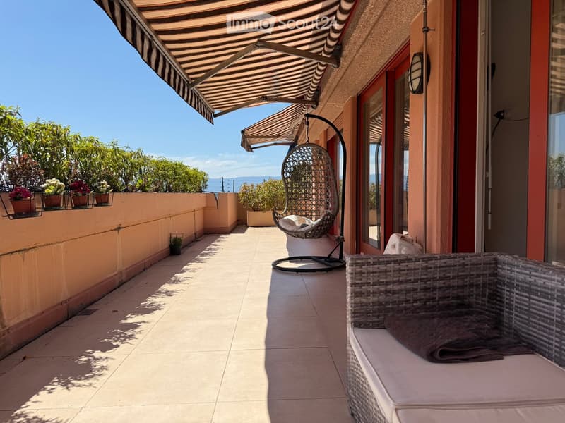 Balcony with tiled floor, wicker seating, hanging chair, and potted plants, overlooking the sea.