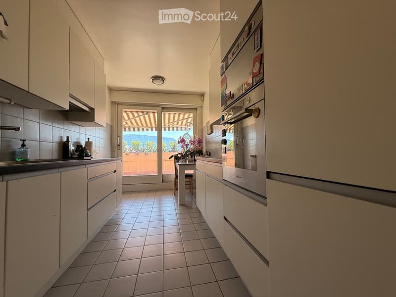 Modern kitchen with white cabinets, stainless steel appliances, tiled floor, and a small dining area leading to a balcony with outdoor seating.