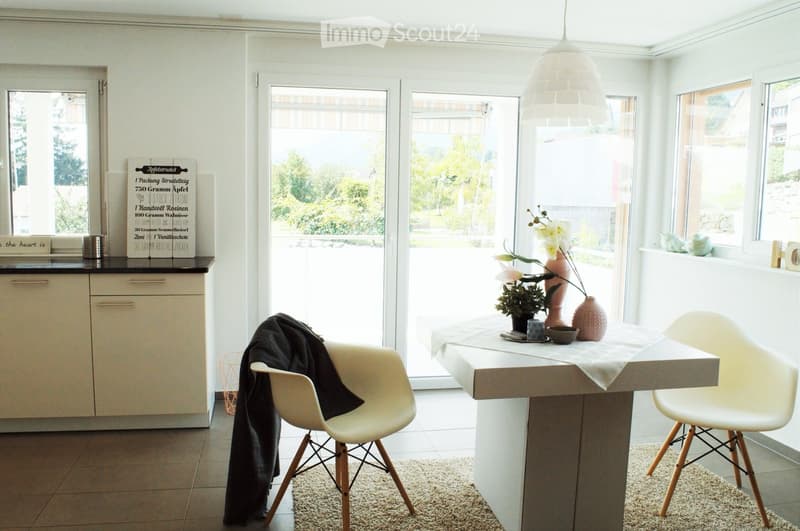 Modern kitchen with white cabinets, a central island table, two white chairs, a vase with flowers, a bowl, and a sign on the counter.