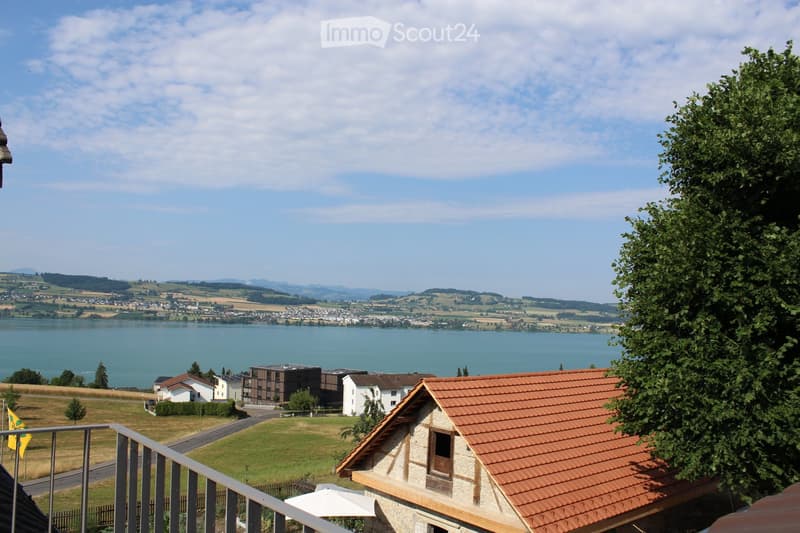 Balcony overlooking a scenic landscape with a lake, distant town, and surrounding hills.