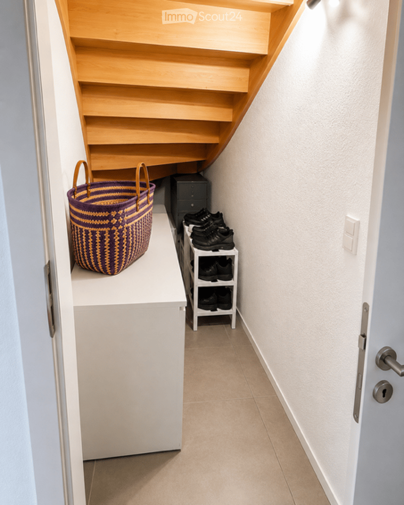 A modern hallway with a wooden staircase, white walls, and a small shelf holding a woven basket and shoes.