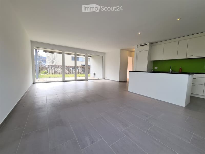 Empty room with tiled floor, white walls, large sliding glass doors leading to outdoor area, and a small kitchen area with cabinets and countertop.