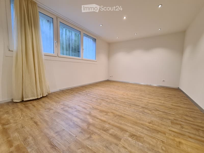 Empty room with wooden flooring, white walls, and large windows with curtains.