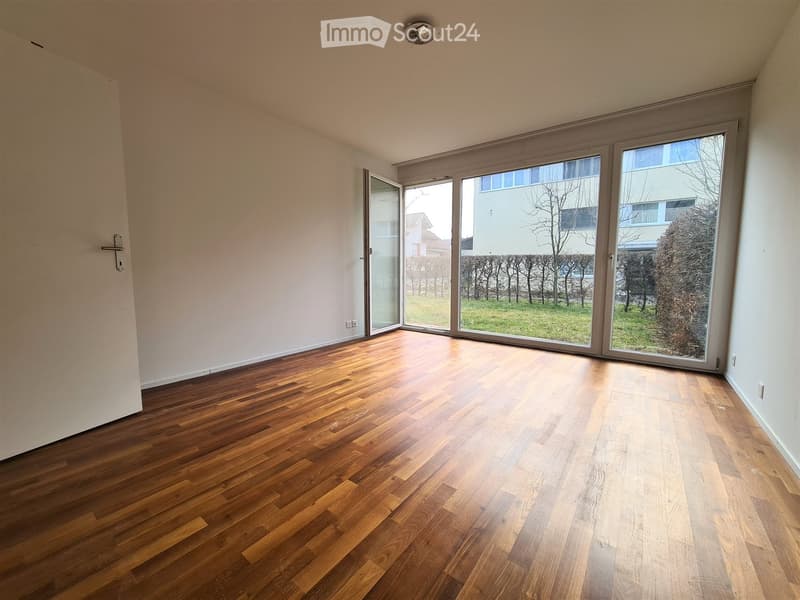 Empty room with wooden flooring, large windows, and a door leading outside.