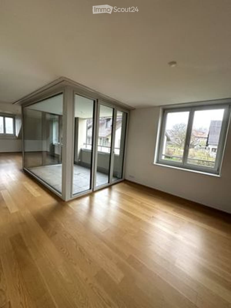 Bright, unfurnished room with wooden flooring, large windows, and a glass balcony door leading to a balcony.
