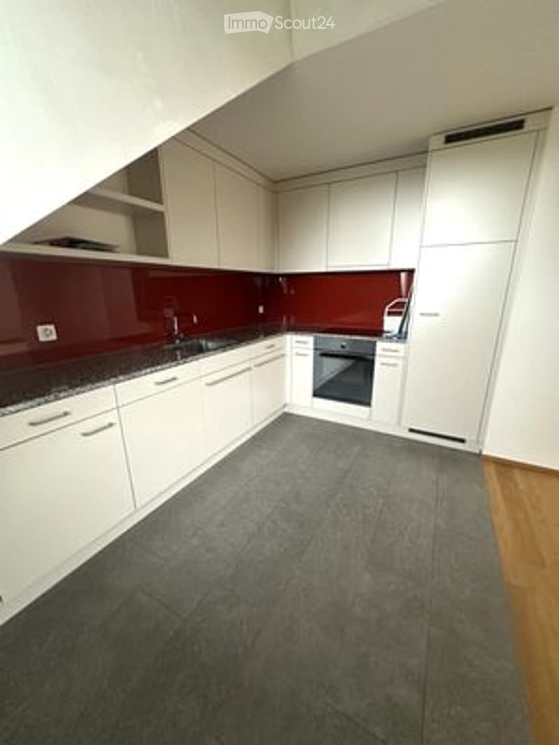 Modern kitchen with white cabinets, dark countertops, and a grey tiled floor. Features a sink, oven, and refrigerator.