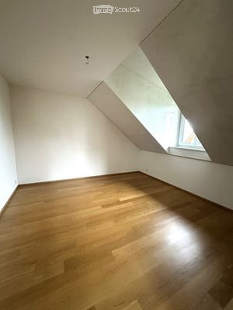 Completely empty room with wooden flooring and white walls, featuring a skylight window at the far end.