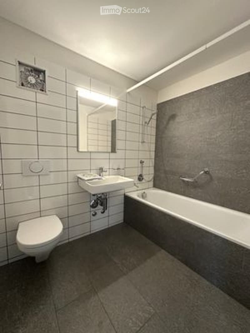 Modern bathroom with white tiled walls, a bathtub, toilet, sink, and a large mirror above the sink.