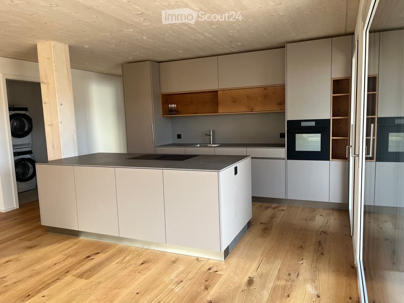 Modern kitchen with light-colored cabinets, a central island, and a built-in oven. The space features wooden flooring and a sleek, contemporary design.