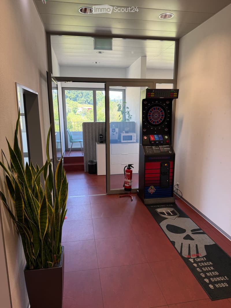 Hallway with red tiled floor, dartboard machine, chair, microwave, and fire extinguisher visible.