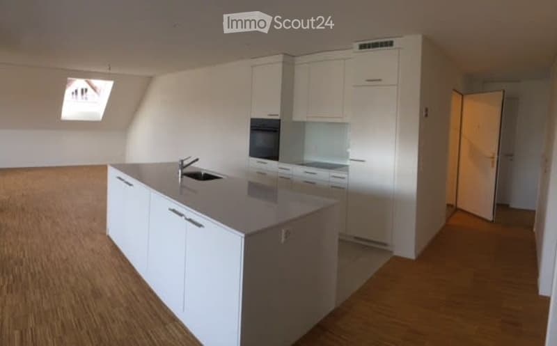 Modern kitchen with white cabinets, a central island, and a sink. The space is bright with wooden flooring and a skylight window.