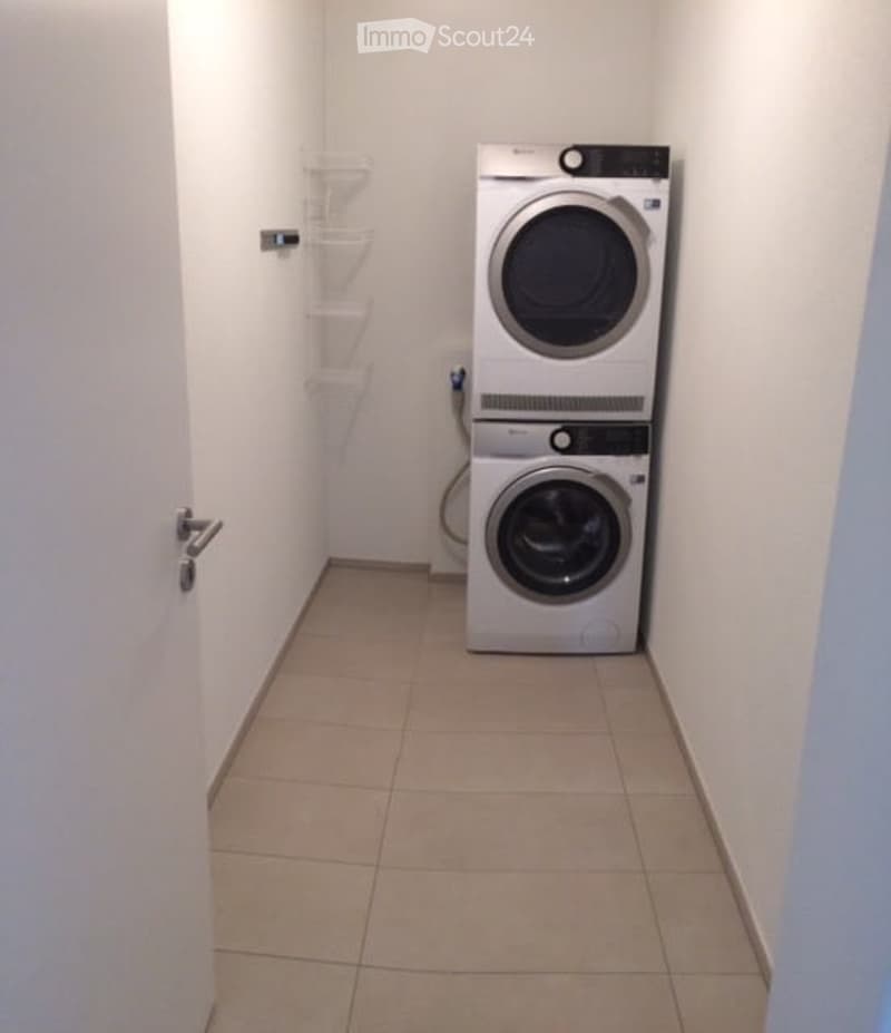 Small, clean laundry room with tiled floor, white walls, and stacked washer and dryer units.