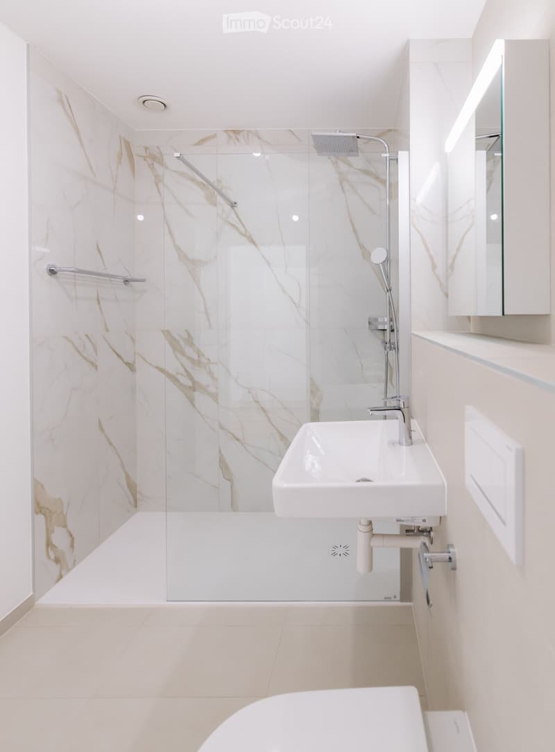 Modern bathroom with white marble tiles, a glass-enclosed shower, a white sink, and a bathtub.