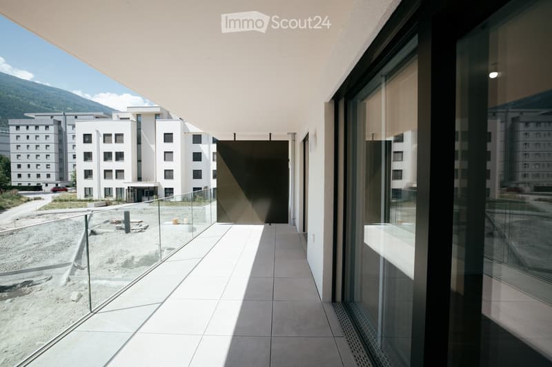 Modern balcony with glass railings, tiled floor, and a view of a construction site and modern buildings in the background.