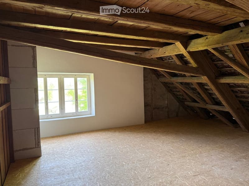 Empty attic space with exposed wooden beams, a single window, and unfinished walls and floor.