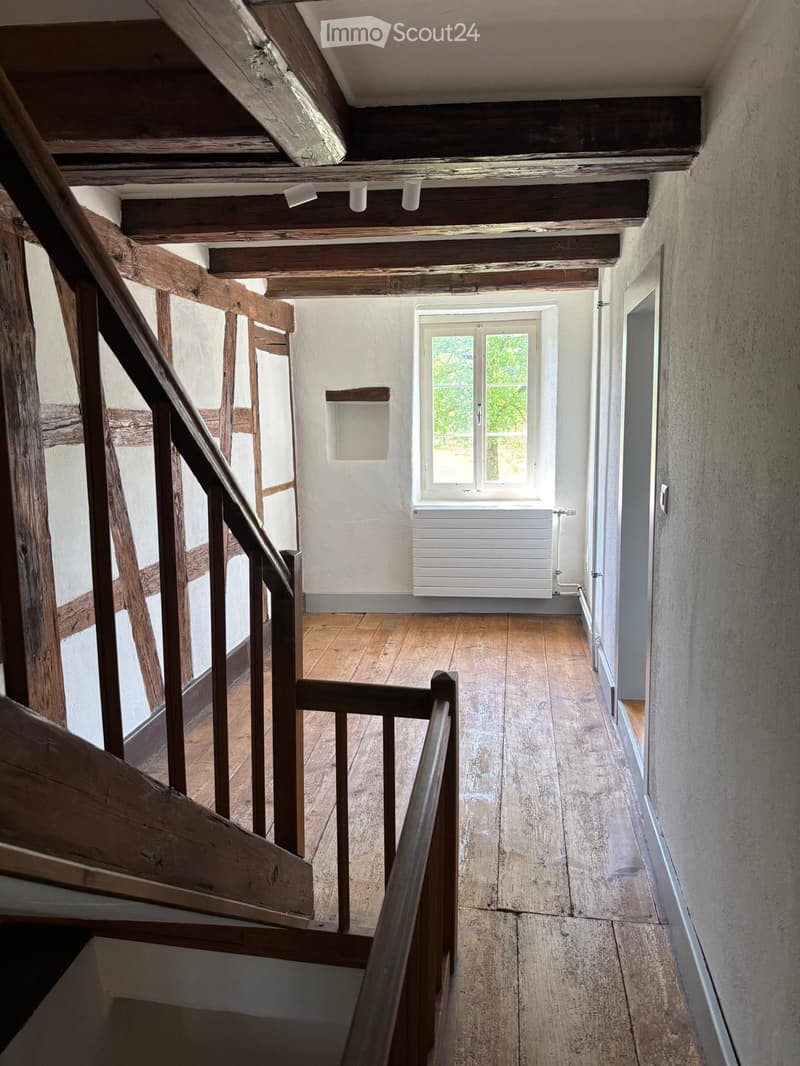Empty wooden hallway with exposed beams, wooden floor, and a window at the end.