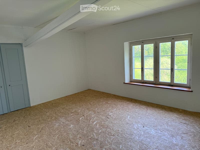 Empty room with light grey walls, wooden floor, single door, and large window with wooden sill.