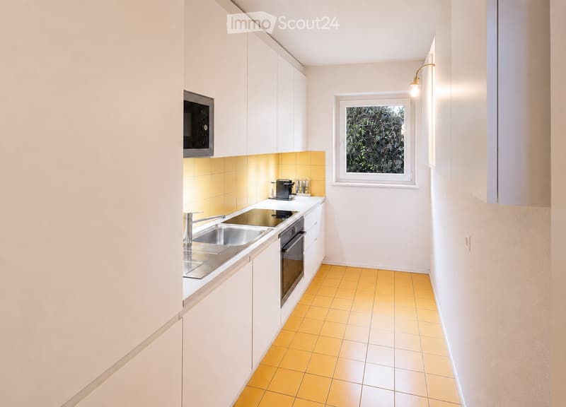 Modern kitchen with white cabinets, stainless steel sink, oven, microwave, and coffee maker. Yellow tiled backsplash and floor.