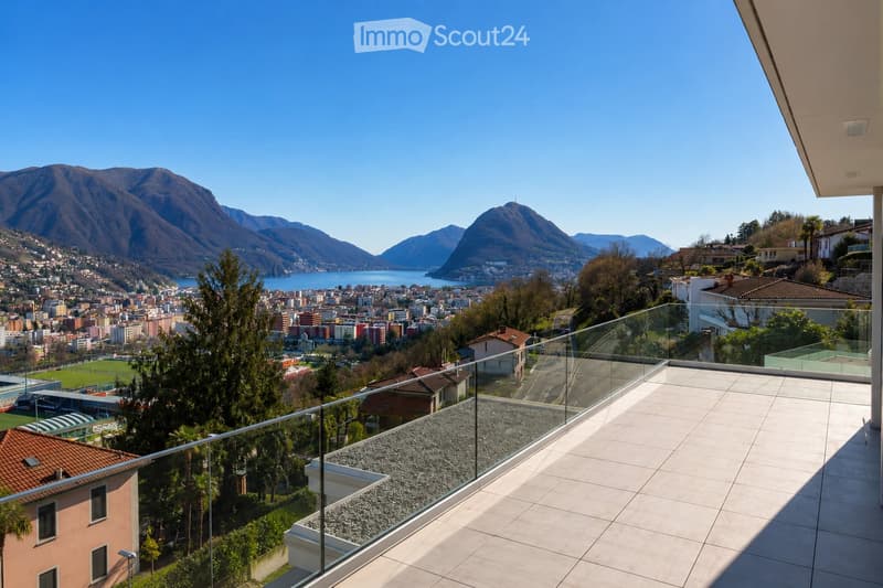 Balcony with modern glass railing, tiled floor, overlooking a scenic lake and mountain view.