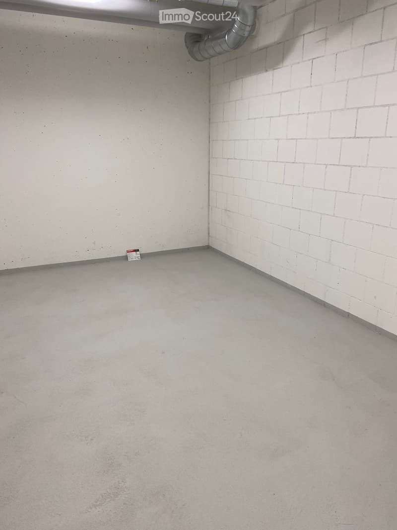 Empty room with concrete floor and white tiled wall, featuring a metal pipe and a small sign on the floor.