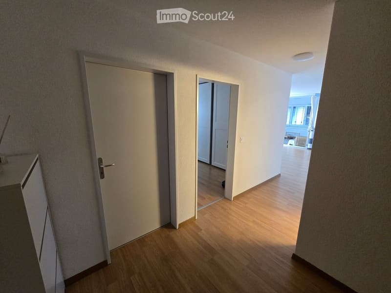Empty hallway with wooden flooring, white walls, and multiple doors leading to other rooms.