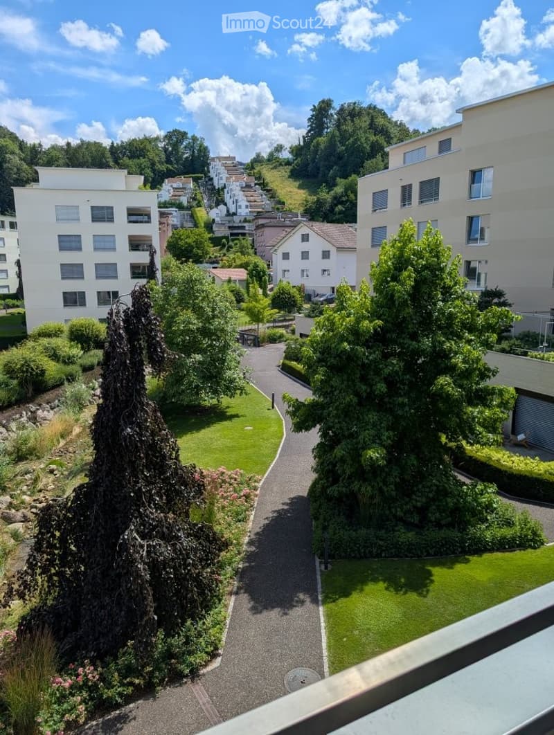 Balcony view of a landscaped garden area with pathways, greenery, and surrounding residential buildings.