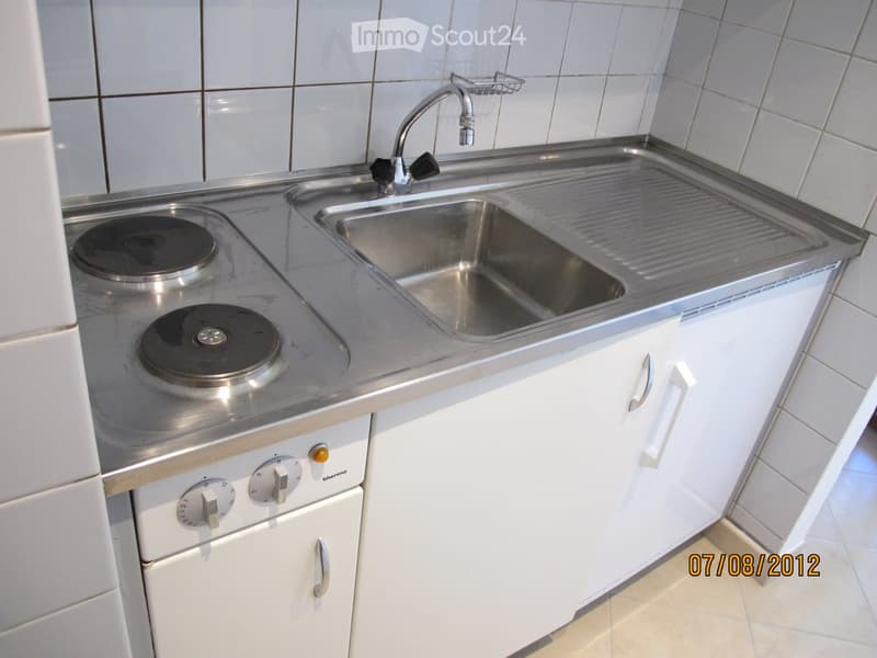 Compact kitchen with a stainless steel sink, faucet, induction cooktop, and white cabinets.