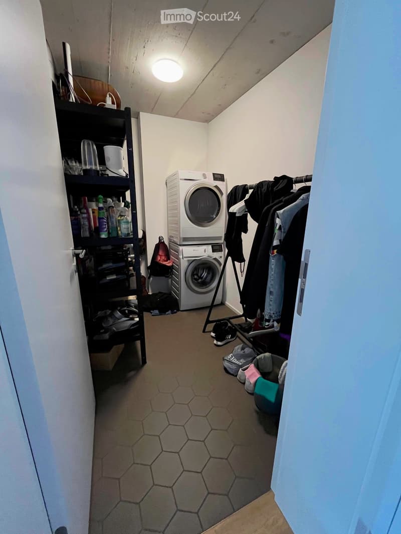 Laundry room with a washing machine, dryer, shelf, and clothing rack.