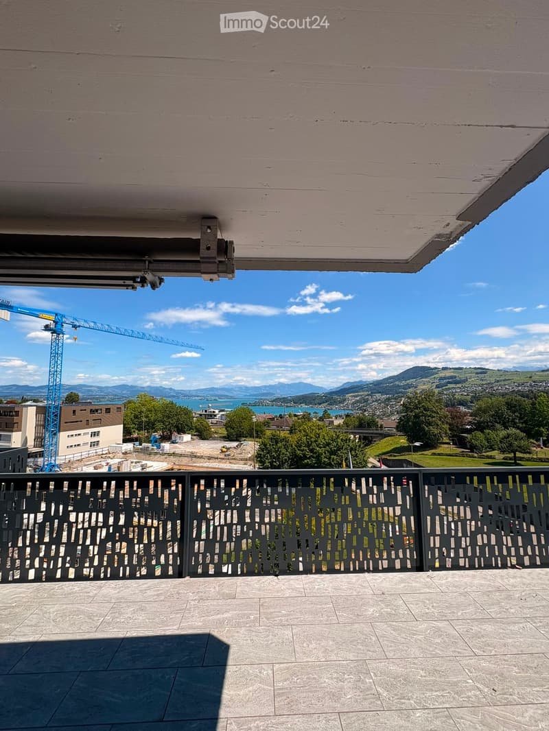 Balcony with modern metal railing, tiled floor, and scenic view of a lake and mountains.