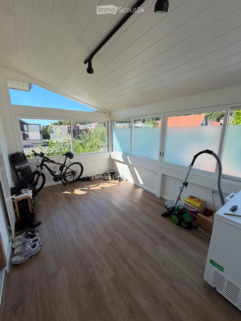 Bright, airy room with wooden flooring, large windows, and skylights. Contains a bicycle, vacuum cleaner, shoe rack, and storage boxes.