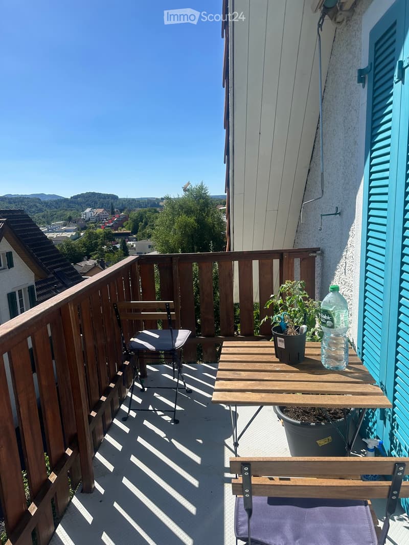 Balcony with wooden railing, table, chairs, bench, potted plants, and a water bottle.