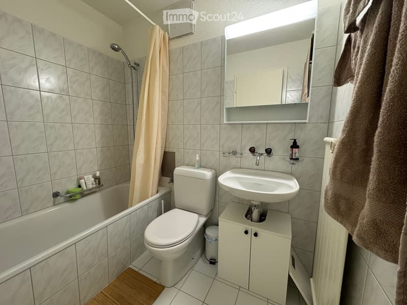 Modern bathroom with tiled walls, a bathtub, toilet, sink, mirror, and a towel hanging on the side.