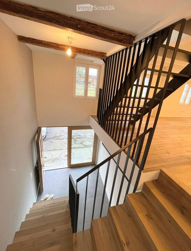 Staircase with wooden steps and metal railing, leading to an open doorway that reveals a paved outdoor area.