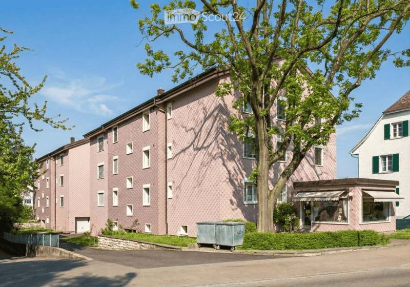 A multi-story residential building with pink siding, multiple windows, and a small storefront at the ground level.
