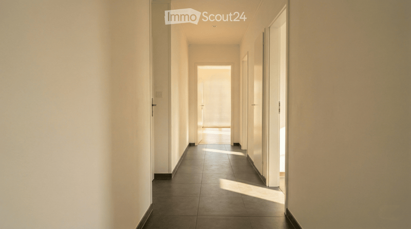 Empty hallway with white walls, dark tiled floor, and several doors leading to other rooms.