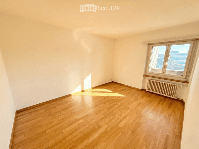 Empty room with wooden flooring and white walls, featuring a large window with a radiator below it.